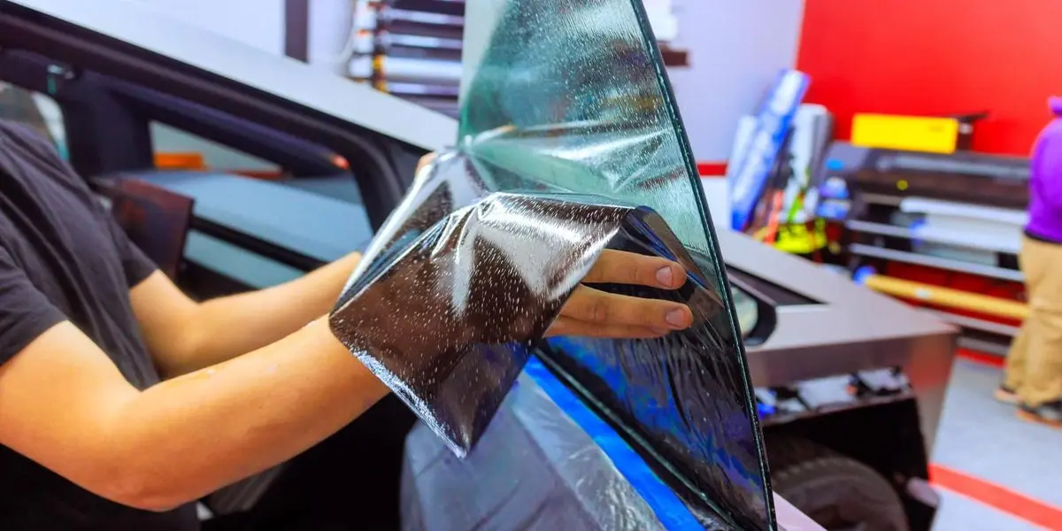 Auto detailing professional using a heat gun to safely remove old bubbling film from a rear car window.
