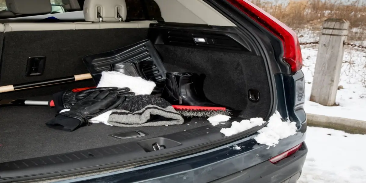 Winter car emergency kit supplies laid out including jumper cables, shovel, and blanket