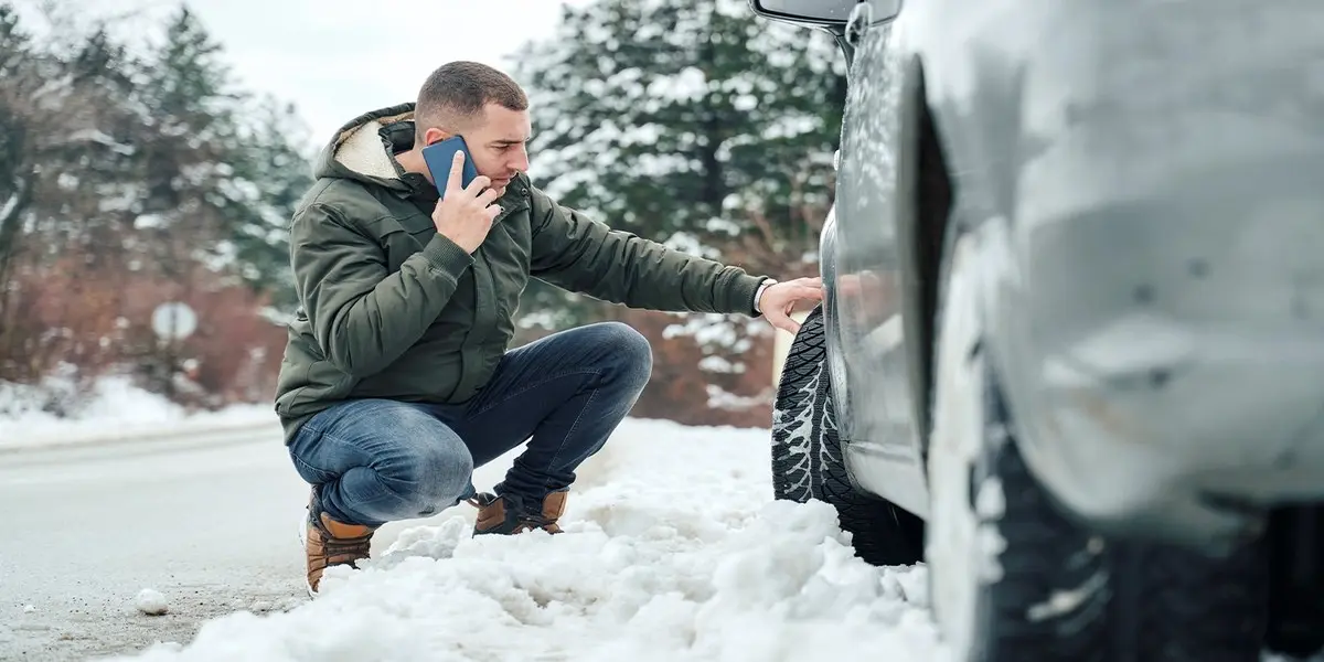 Checking tire pressure with a gauge on a snow-covered tire during winter.