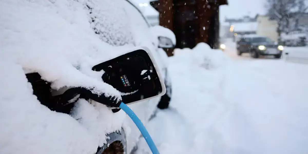 An electric vehicle connected to a charger at a public charging station in snow.