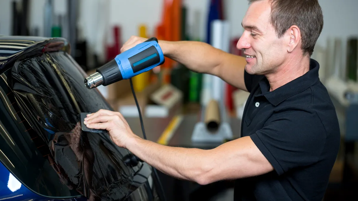 Professional window tint installer using a precision squeegee tool to apply tint film to a vehicle door glass.