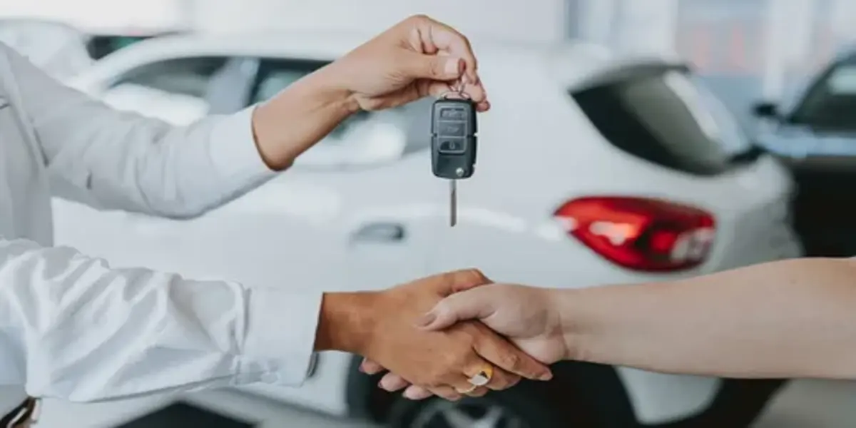 A buyer and seller shaking hands over a car key and price paperwork during a used Toyota Corolla sale.