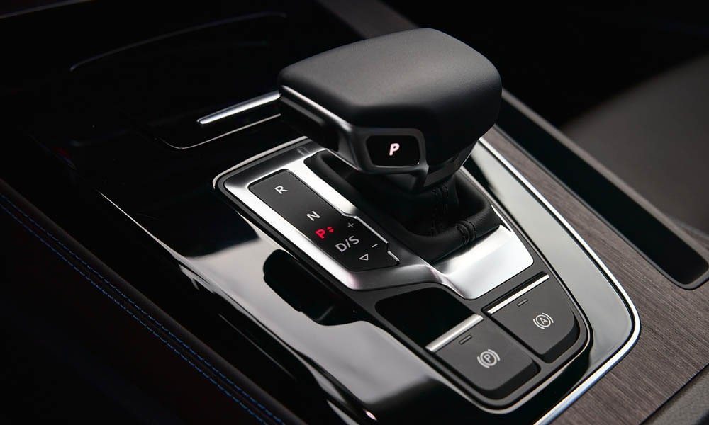 Close-up of an Audi automatic gear shifter, electronic parking brake switch, and dark wood trim on the center console.