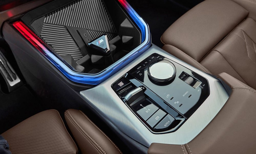 Close-up of a BMW center console with an iDrive controller dial, gear selector, and illuminated wireless charging pad.