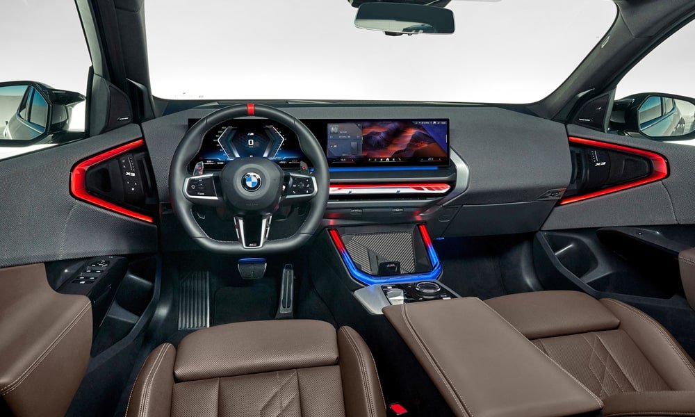 Interior cockpit view of a modern BMW X3 showing the leather steering wheel, curved digital displays, and vibrant red and blue ambient ambient lighting.