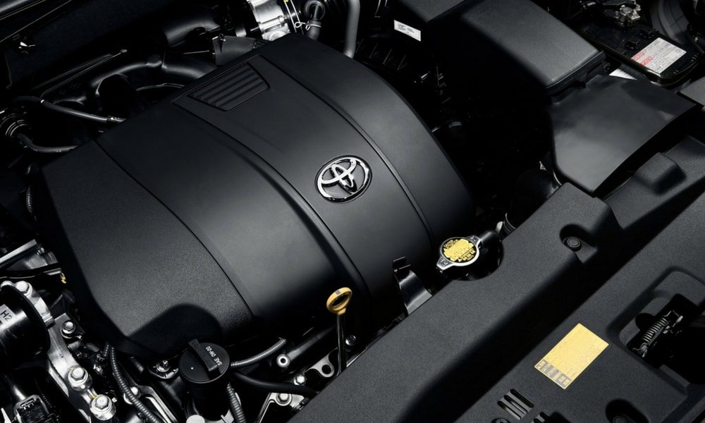 Toyota engine bay showing a black engine cover with the Toyota logo, oil dipstick, coolant cap, air intake, and surrounding components.