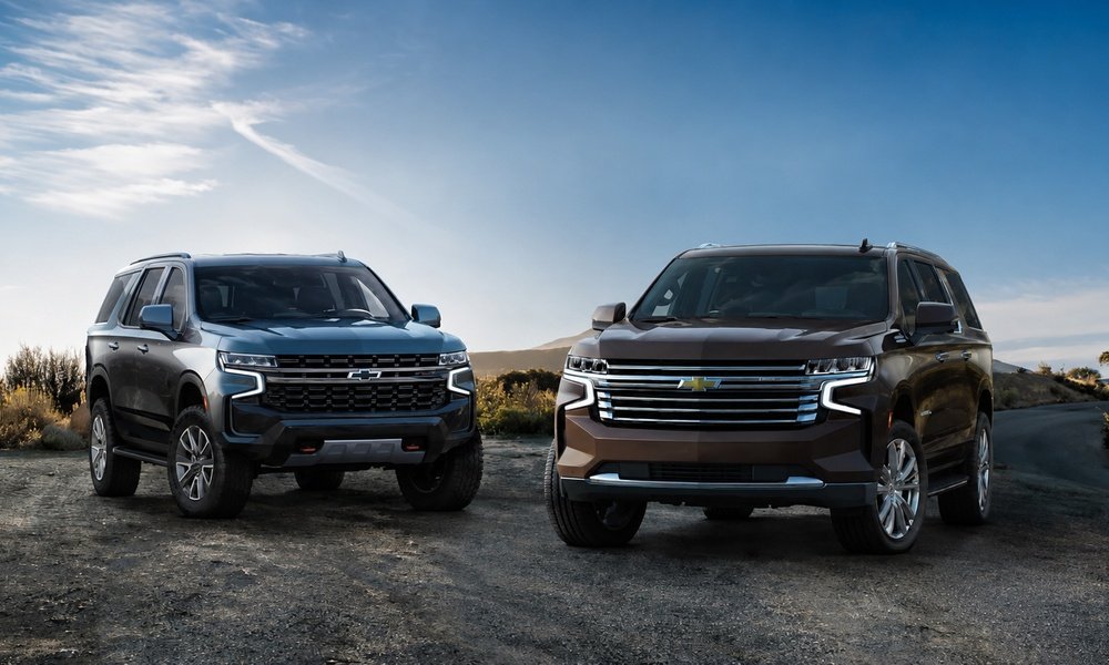 Two Chevrolet SUVs parked side by side on a rugged road with hills and a blue sky in the background.