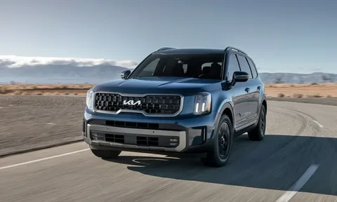 A blue Kia Telluride SUV driving along a paved road in a desert landscape.