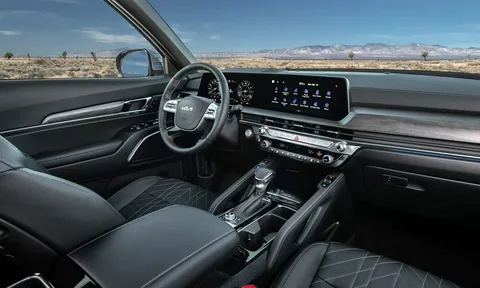 The interior front dashboard and steering wheel of a modern Kia SUV featuring dual digital display screens and black leather seating.