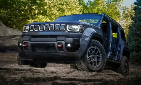 A dark blue-gray Jeep Recon electric SUV with doors removed, driving over rocky terrain outdoors.