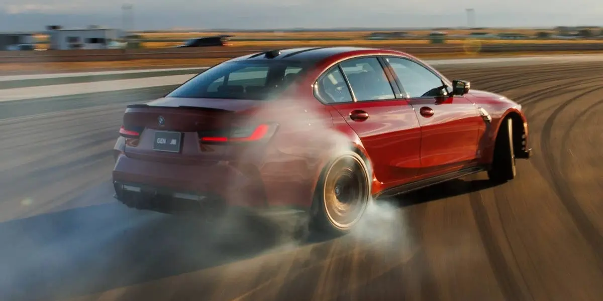 Red BMW M3 high-performance sedan drifting on a racetrack with tire smoke.