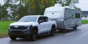 A Chevrolet Silverado towing a substantial travel trailer on a highway, with the truck and trailer both clearly visible.