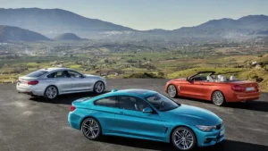 Three BMW 4 Series body styles including a turquoise Coupe, silver Gran Coupe, and orange Convertible parked on a scenic overlook